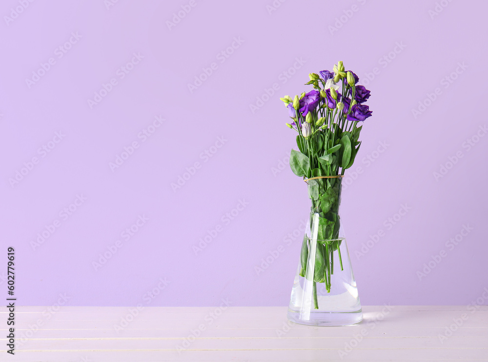 Vase with eustoma flowers on wooden table near lilac wall