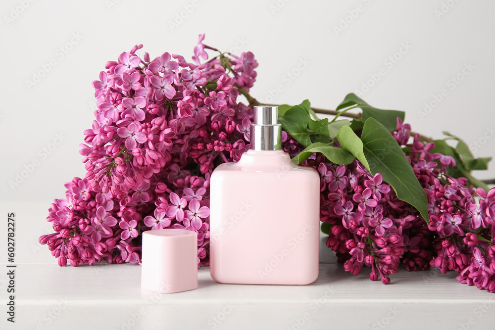 Beautiful blossoming lilac flowers with bottle of perfume on wooden table near white wall