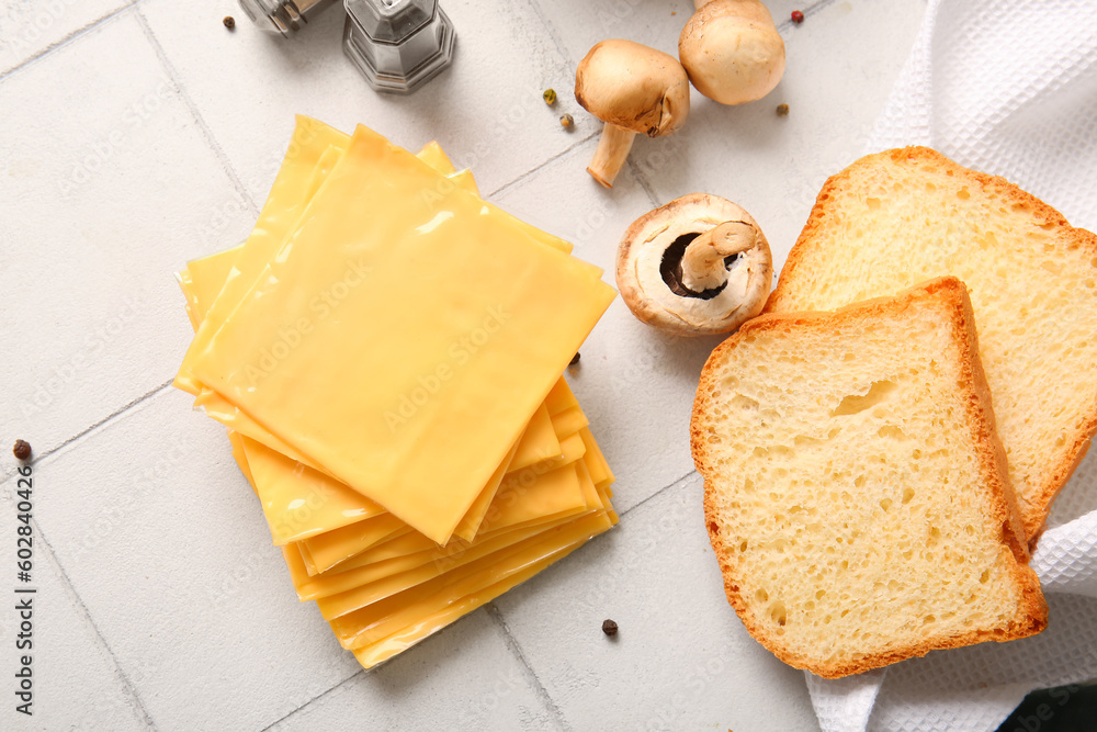 Slices of tasty processed cheese and bread on white tile background