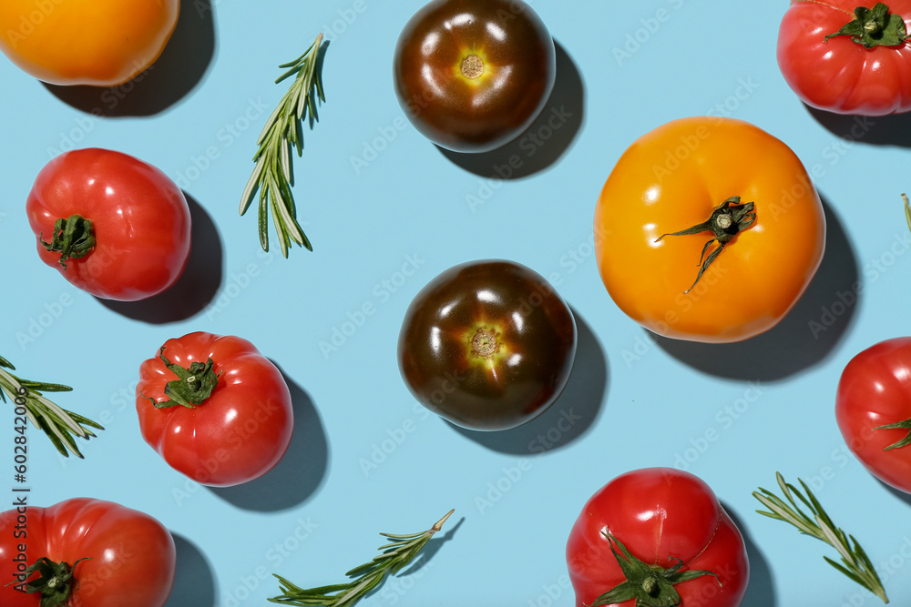 Different fresh tomatoes and rosemary on blue background