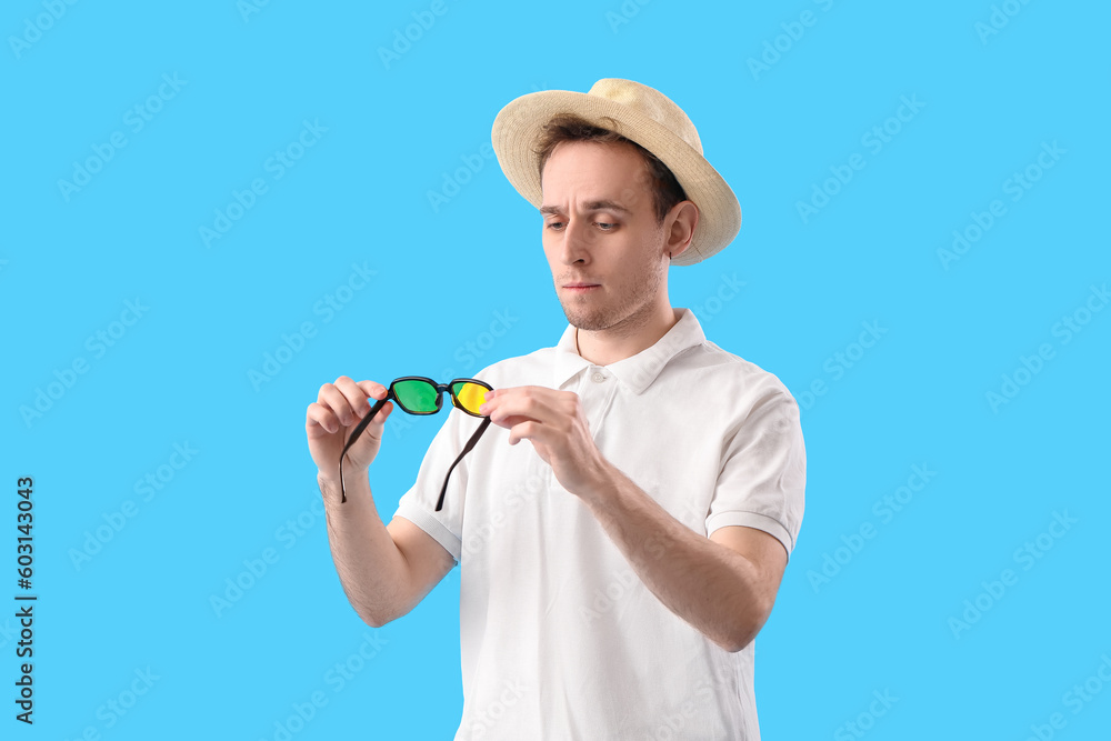 Young man in straw hat with sunglasses on blue background