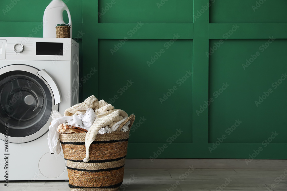 Basket with dirty clothes and washing machine near green wall in laundry room