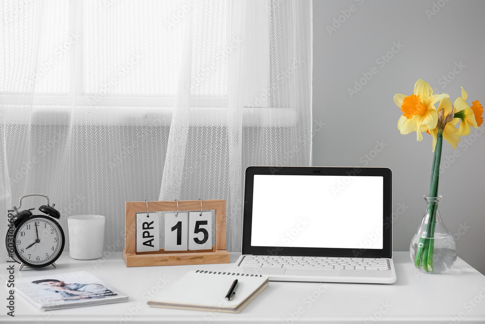 Comfortable workplace with modern laptop and beautiful narcissus flowers near window