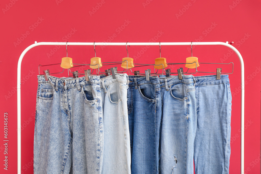 Rack with stylish jeans on red background, closeup