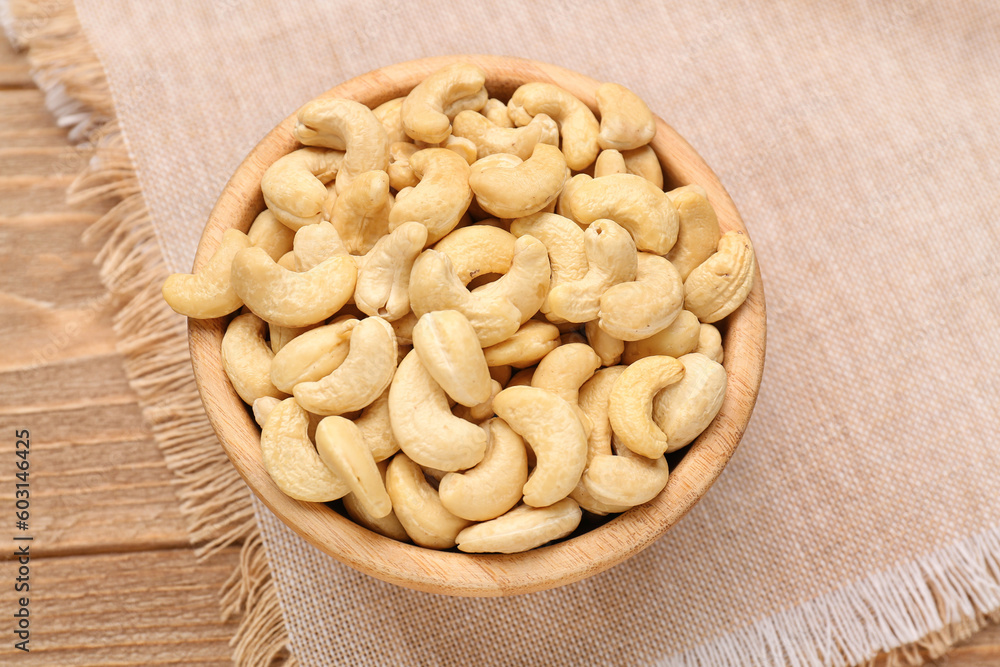 Bowl with tasty cashew nuts on wooden background