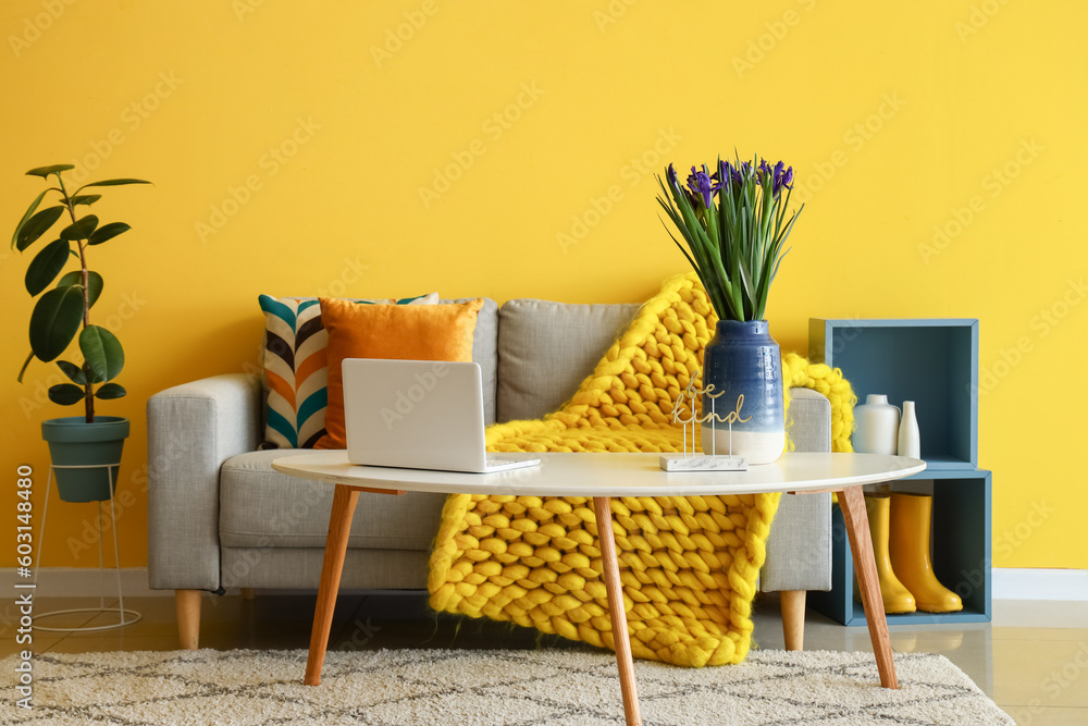 Interior of stylish living room with grey sofa, iris flowers and modern laptop on coffee table