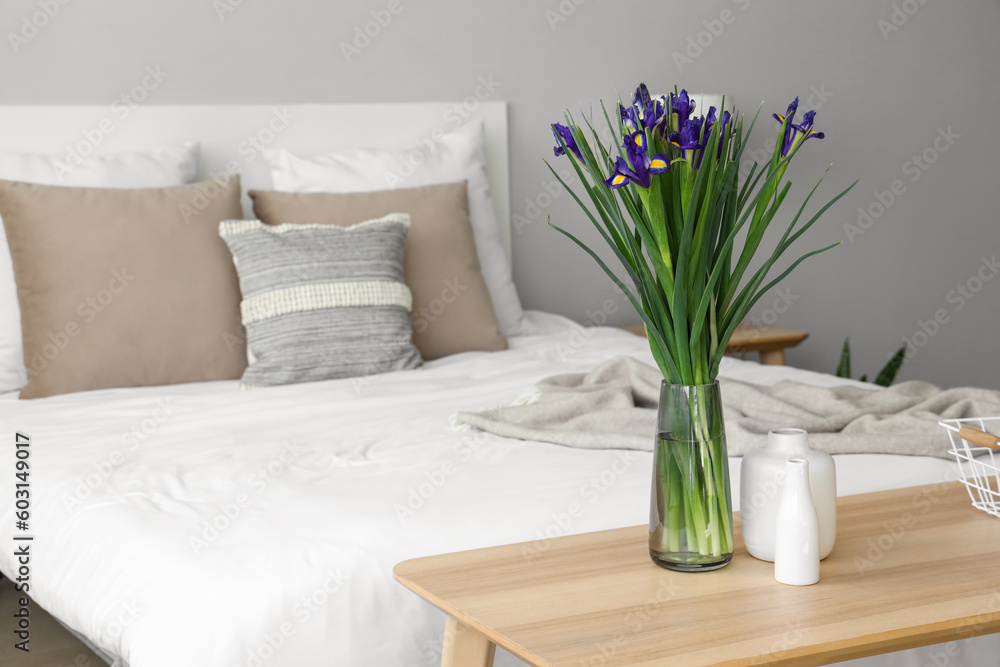 Vase with blooming iris flowers on bedside table