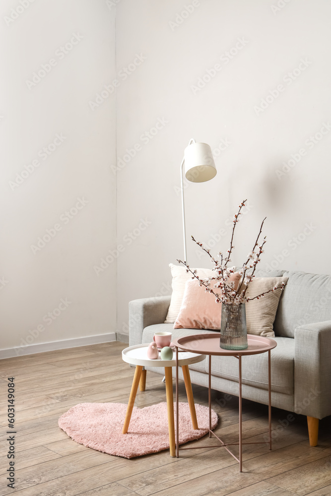 Interior of living room with grey sofa and blooming tree branches on coffee table