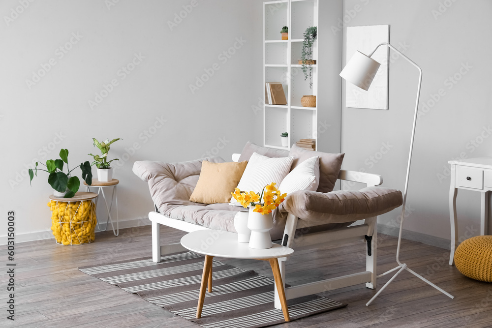 Interior of stylish living room with cozy sofa and blooming narcissus flowers on coffee table