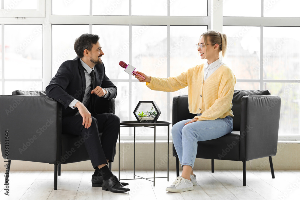 Female journalist with microphone having an interview with man in office