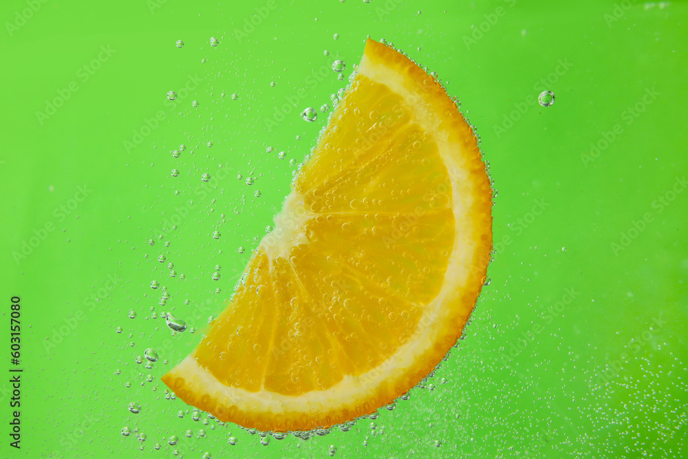 Orange slice in water with bubbles on green background