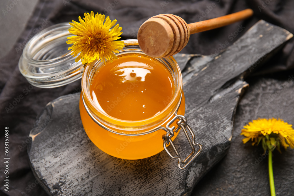 Board and jar with dandelion honey on black background