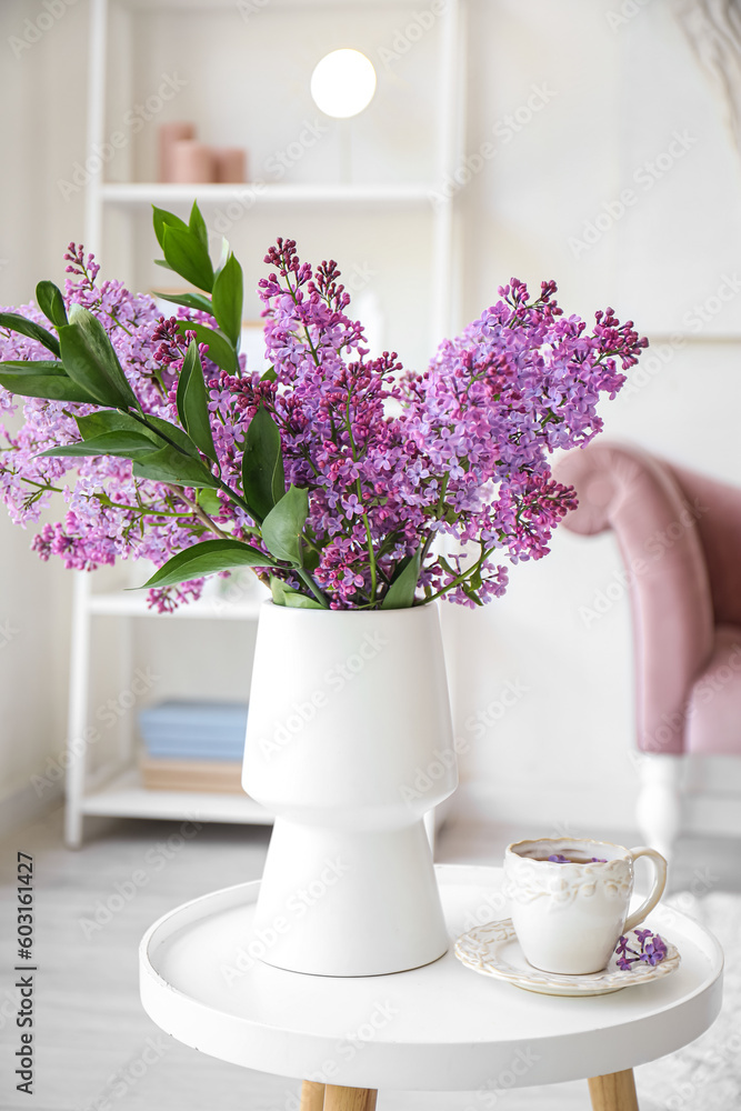 Vase with blooming lilac flowers and cup of tea on coffee table in interior of living room