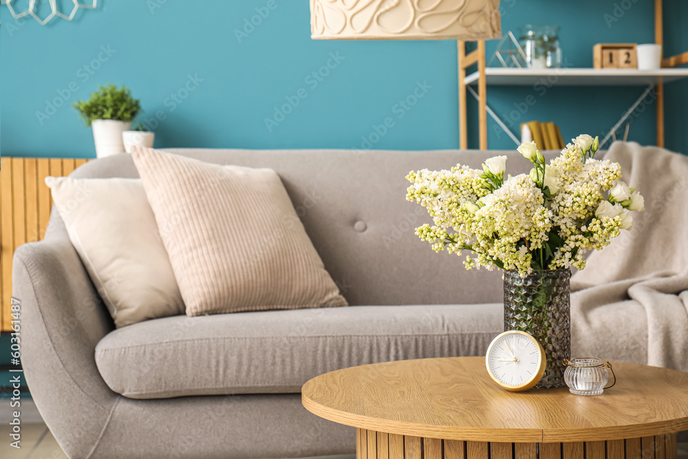 Vase with blooming lilac flowers and alarm clock on wooden coffee table in living room