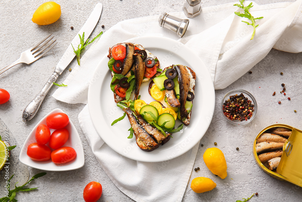 Plate of tasty sandwiches with canned smoked sprats and tomatoes on grey background