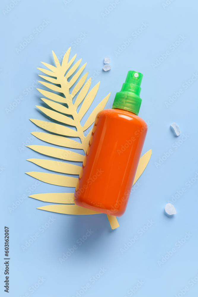 Bottle of sunscreen cream with paper palm leaf on blue background