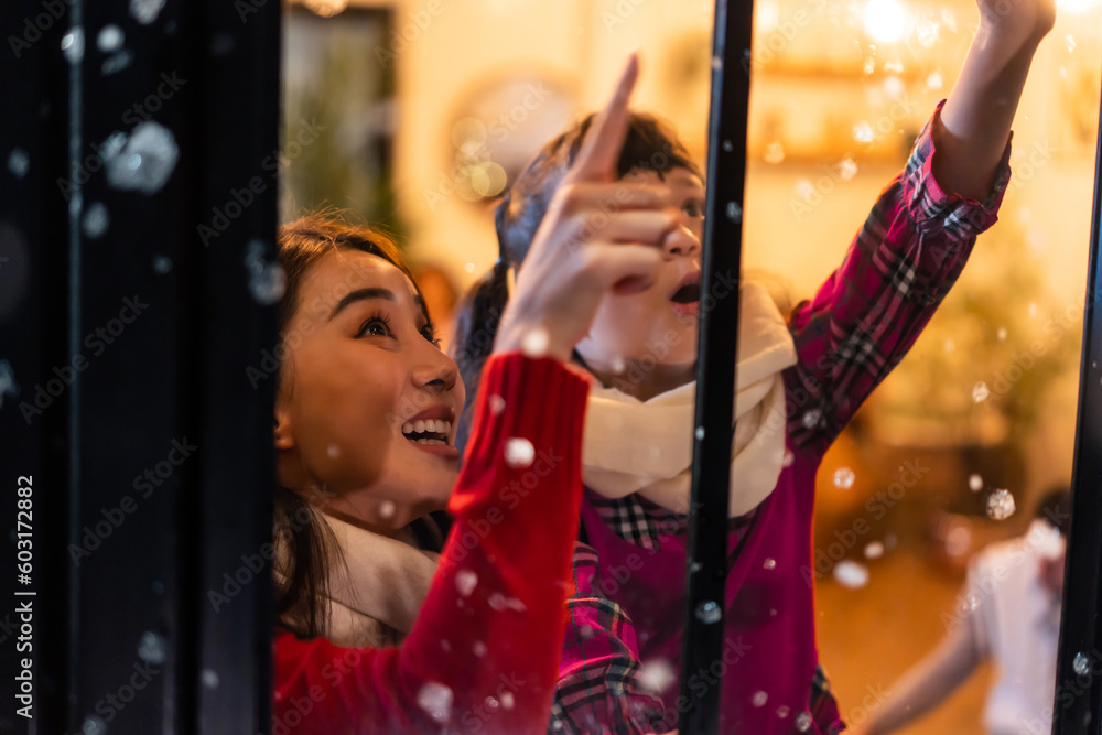 Adorable child looking at the window and first snow flakes with family.