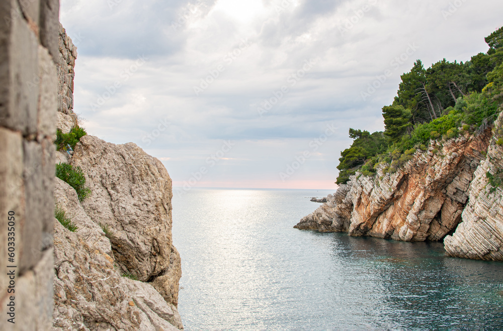 Landscape scenery of coastal rock under forest, calm sea water and stormy clouds in the horizon. Sum