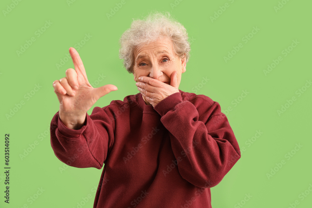 Senior woman showing loser gesture on green background