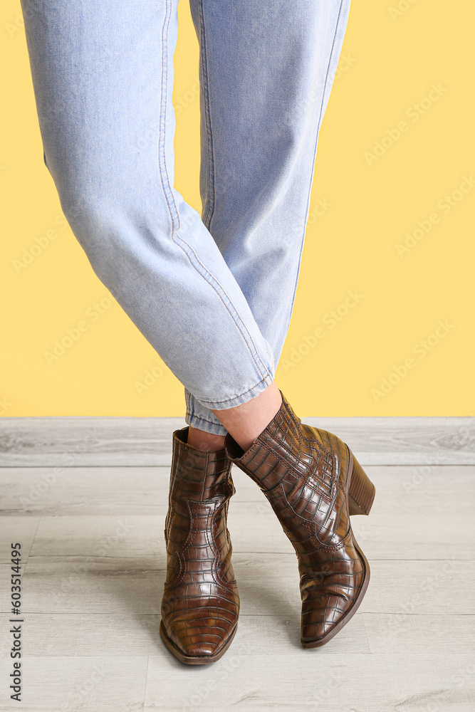 Young woman in stylish jeans near yellow wall, closeup