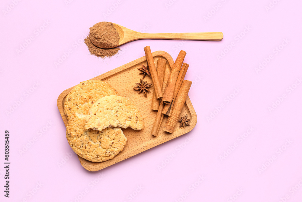 Wooden board with tasty cookies, cinnamon sticks, powder and anise stars on pink background