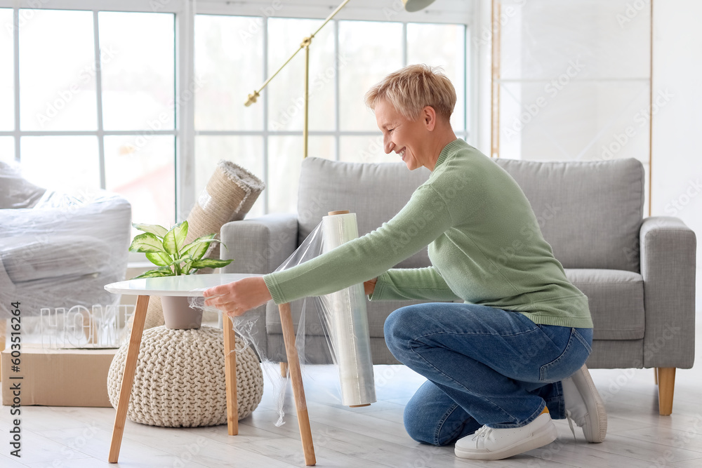 Mature woman wrapping table with stretch film at home