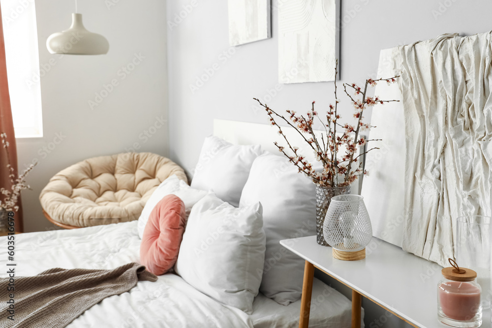 Vase with blooming tree branches on bedside table