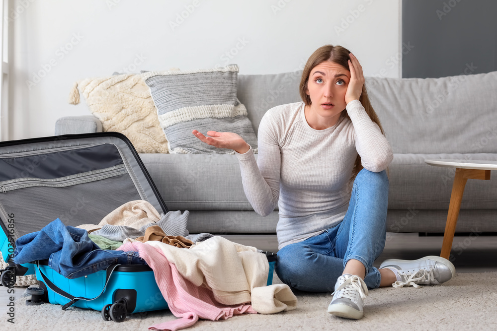 Stressed young woman unpacking suitcase at home