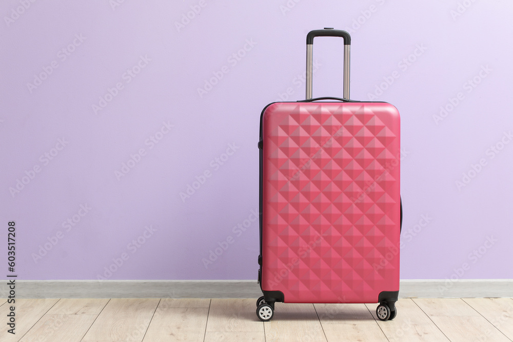 Pink suitcase near lilac wall