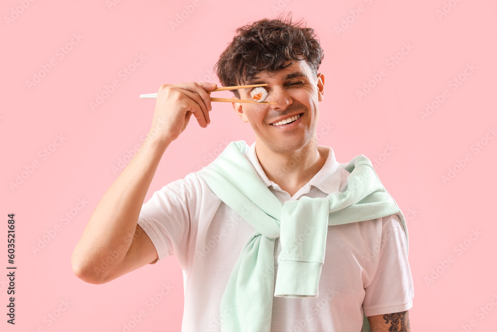 Young man with sushi roll on pink background