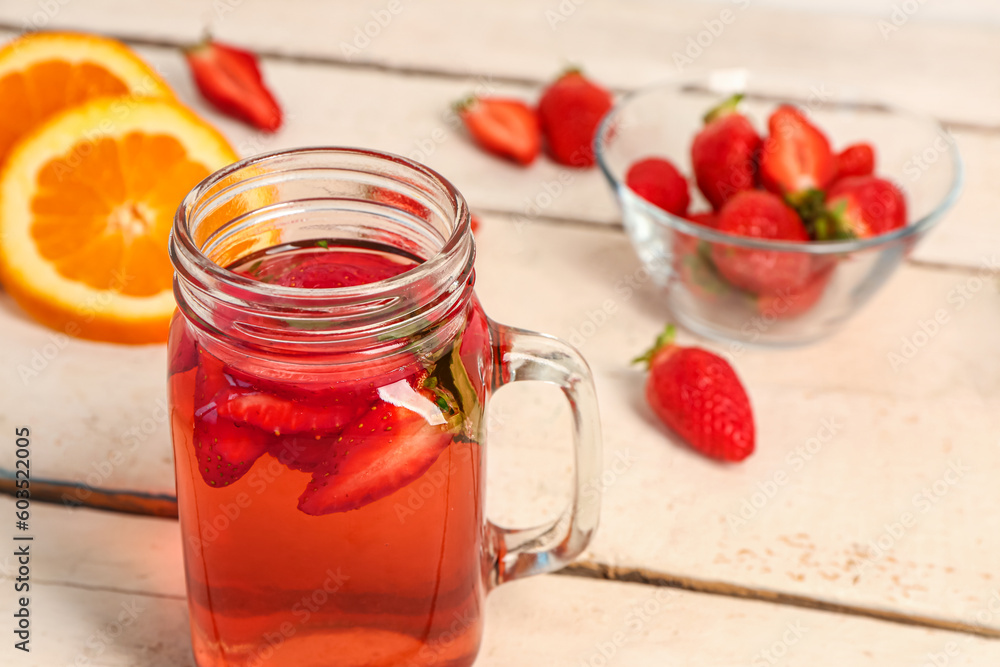 Mason jar of juice and bowl with strawberry on white wooden table