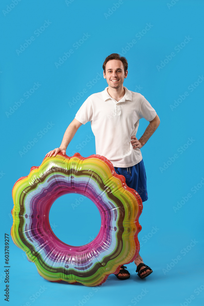 Young man with inflatable ring on blue background