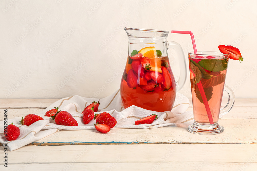 Glass and jug of tasty strawberry juice on white wooden table