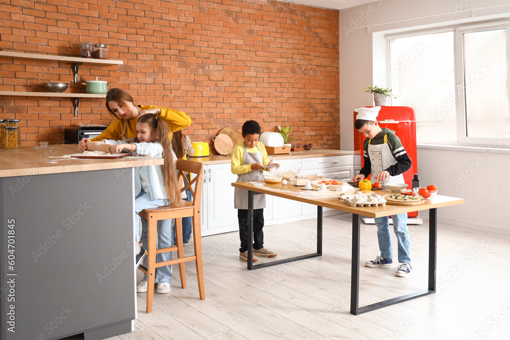 Female chef with group of little children preparing pizza during cooking class in kitchen