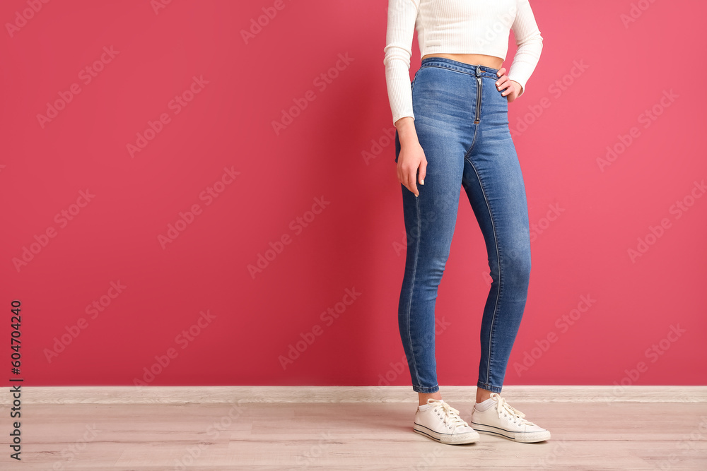 Young woman in stylish jeans near red wall