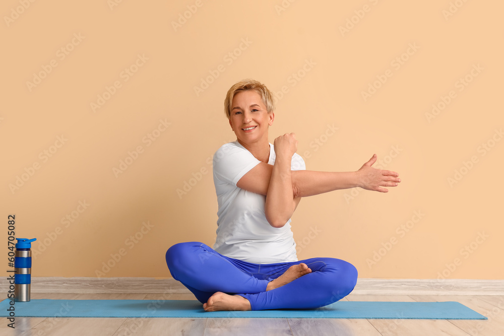 Sporty mature woman practicing yoga against beige wall