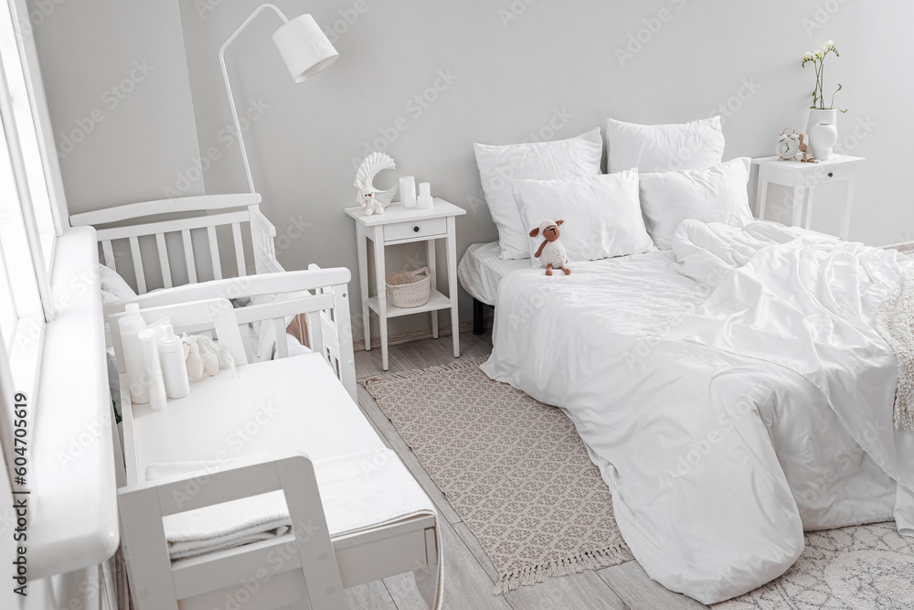 Interior of light bedroom with bed, changing table and baby crib