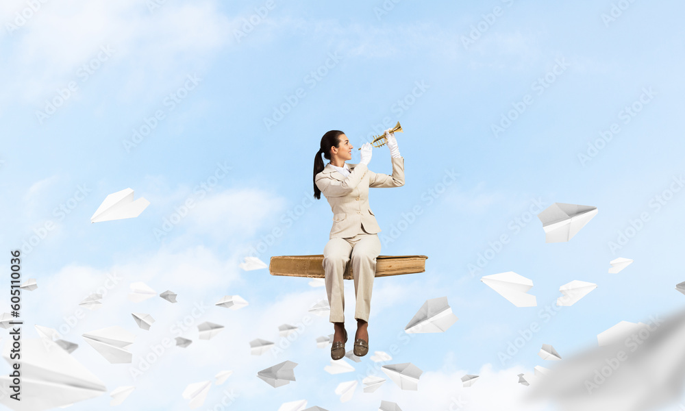 Young woman playing trumpet and sitting on book