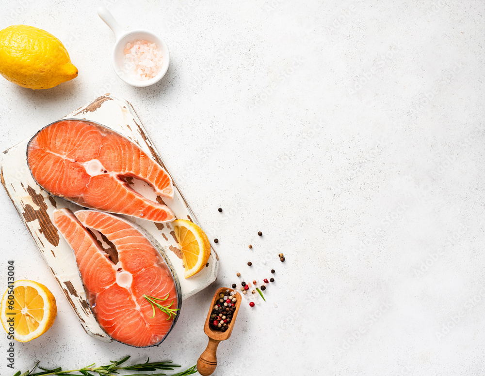 Fresh raw salmon steaks with spices and lemons on wooden board. Top view of fish on white background