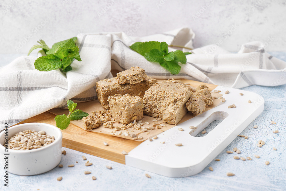 Board with pieces of tasty halva and sunflower seeds on light background