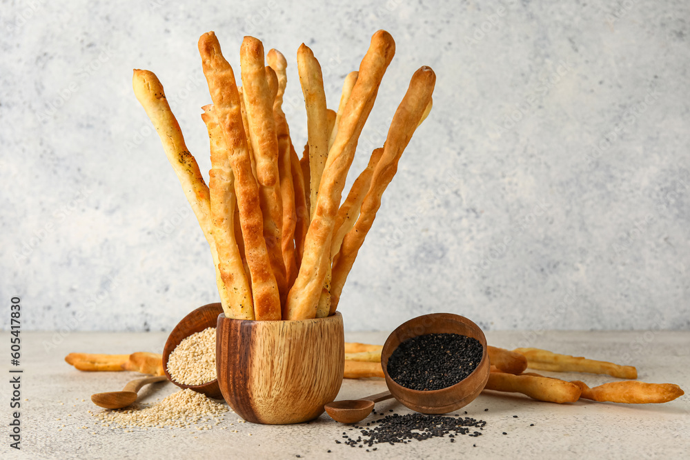 Wooden bowl with tasty Italian Grissini and sesame seeds on light background