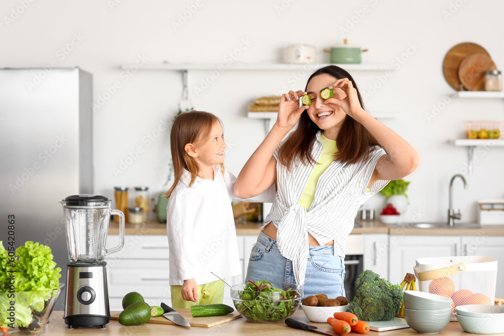 Little girl with her mother and cucumber slices having fun in kitchen