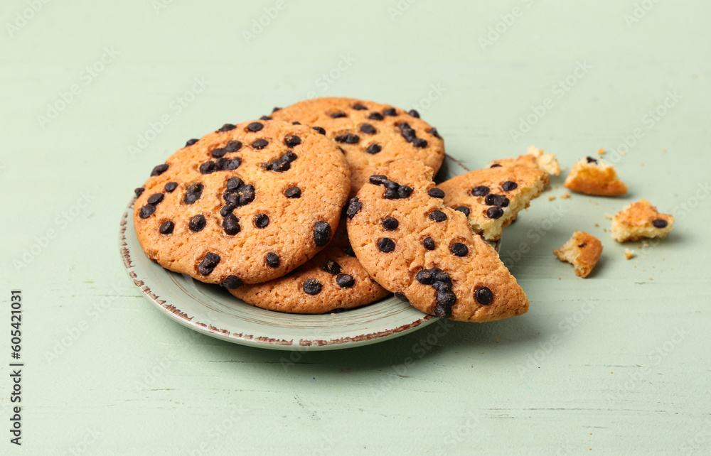 Plate of tasty cookies with chocolate chips on green wooden background