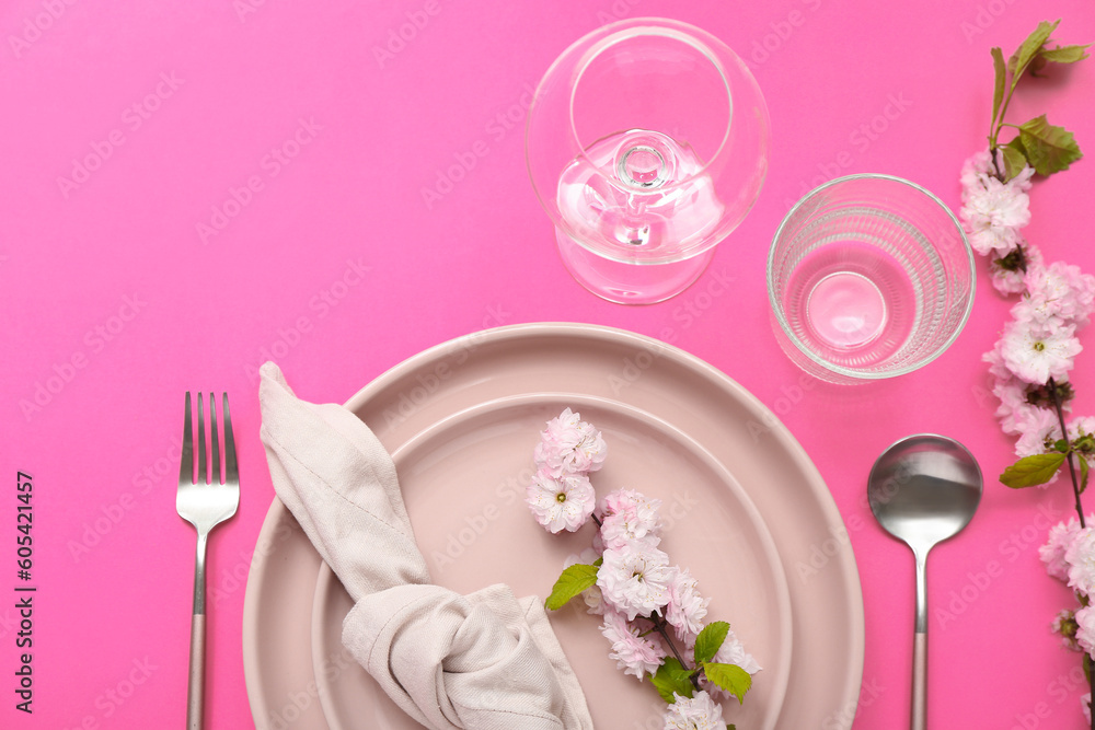 Beautiful table serving with cutlery, blooming tree branches and folded napkin on pink background