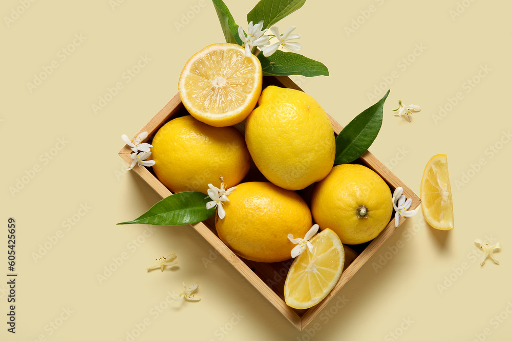 Wooden box of lemons with blooming branch on beige background