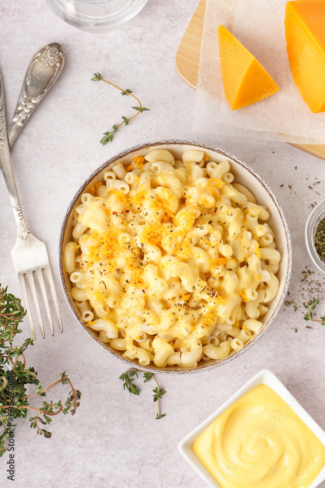 Bowl of tasty Italian pasta with Cheddar cheese on light background