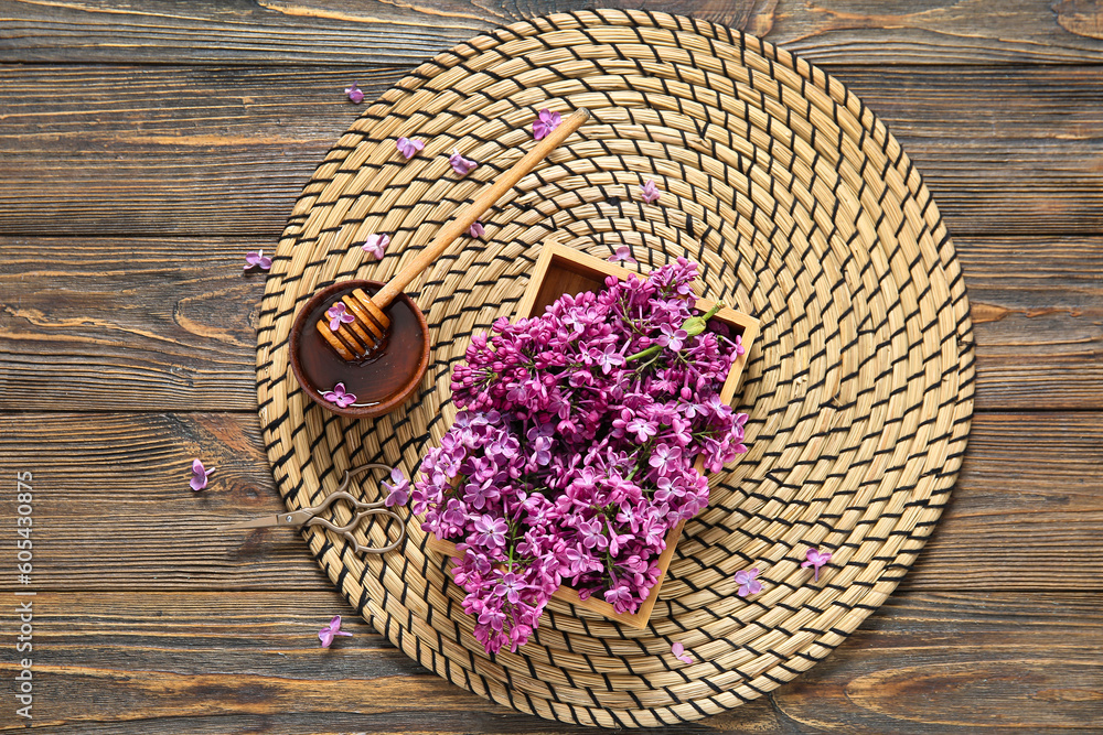 Wicker mat and box of beautiful lilac flowers with honey on brown wooden background