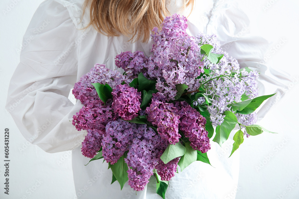 Young woman holding bouquet of beautiful lilac flowers near white wall