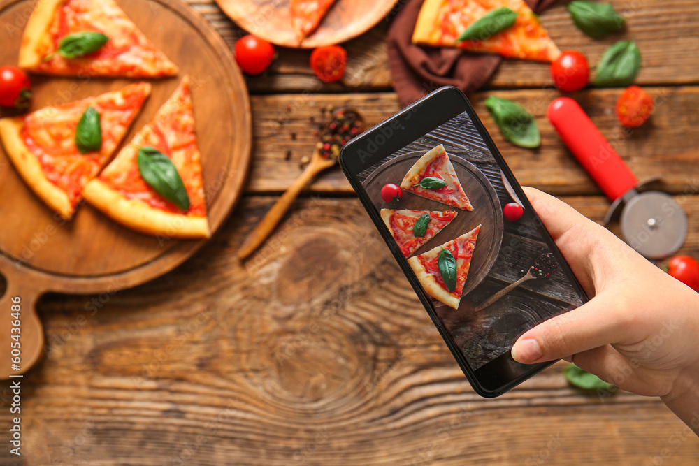 Woman taking photo of tasty pizza margarita on brown wooden background