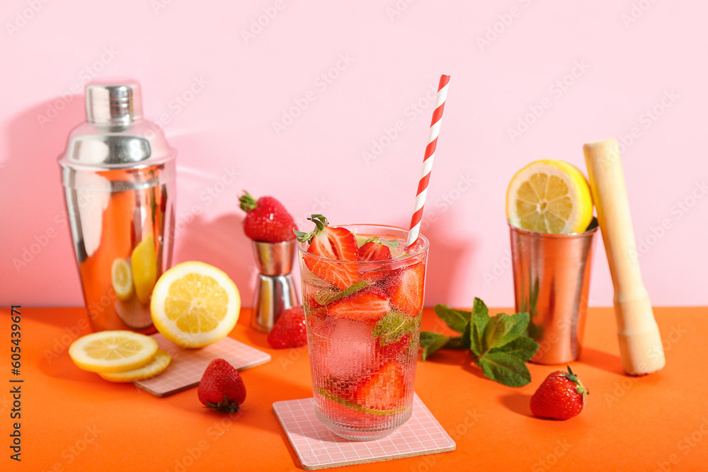 Glass of fresh strawberry mojito with shakers, pestle and jigger on orange table near pink wall